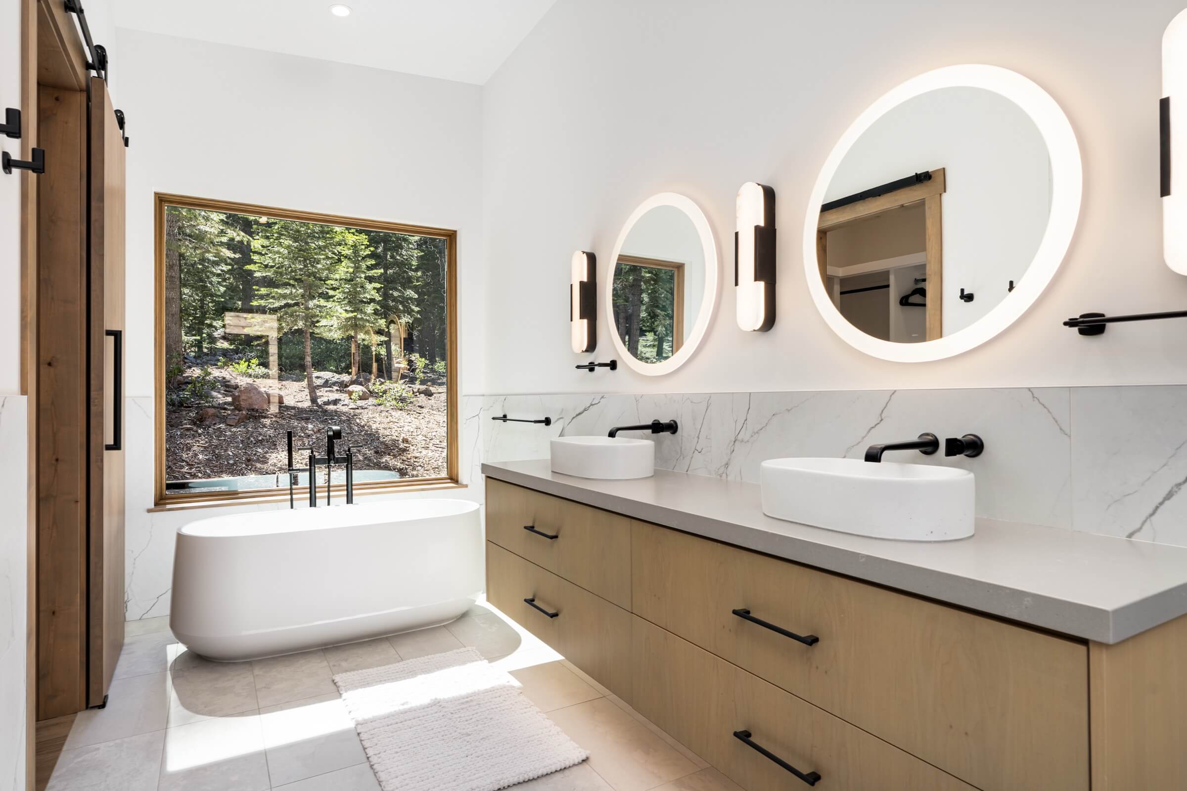 Modern bathroom in Truckee with double sink vanity, round mirrors, and a bathtub.
