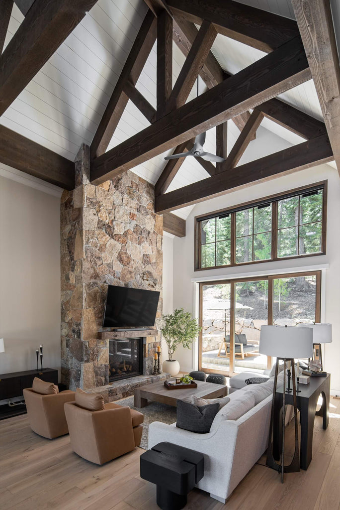 Modern living room with stone fireplace, large windows, and wooden beams.